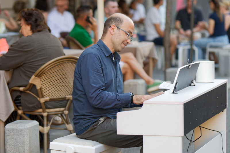 Man in a patterned blue button-down shirt playing a digital piano on a cafe terrace